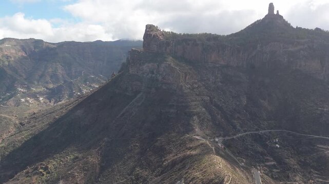 A captivating aerial drone shot of the majestic Roque Nublo rock formations on Gran Canaria. The drone pans right, revealing the island's rugged volcanic landscape and lush valleys.
