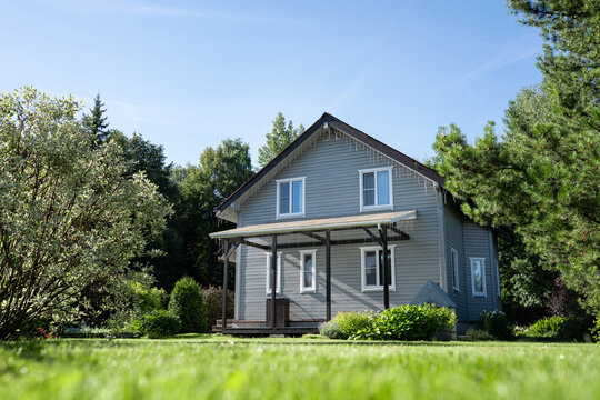 Russian dacha country house surrounded by lush green garden on sunny summer day. Concept of countryside living, summer vacation, gardening and peaceful life outside the city.