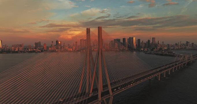 4k aerial view of Mumbai Sea link during orange blue sunset in Monsoon. Beautiful golden hour view of the Mumbai city skyline and Arabian Sea with cars running on the bridge. Cityscape of skyscrapers