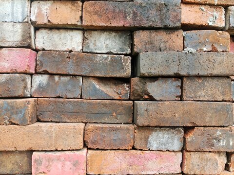 Close-up texture of stacked weathered red clay bricks showing rough surfaces, aging, and natural color variations
