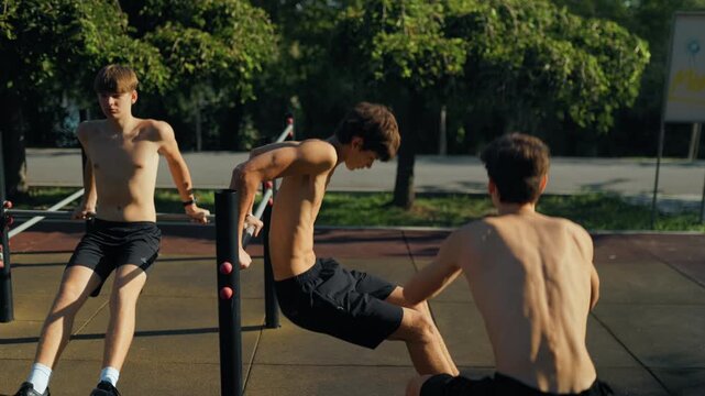 Shirtless Adolescent boys doing triceps dips on parallel bars at the sports ground.
