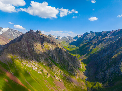 Aerial View of Mountain Valley with Green Slopes and Snow-Capped Peaks