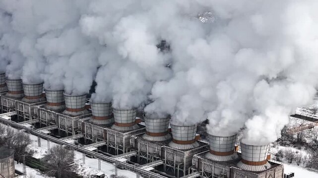 Aerial view of a row of industrial smokestacks emitting smoke, polluting the air, and accelerating climate change and the climate crisis.
