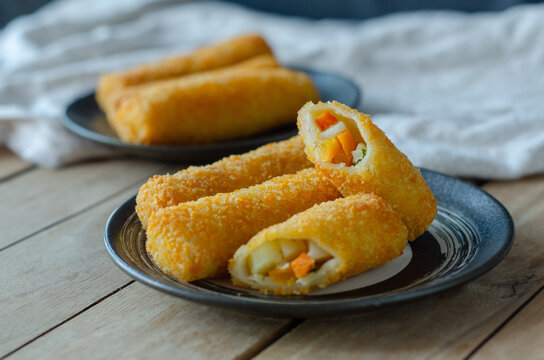 Indonesian risoles, crispy breaded fried snacks served on black plates over a wooden table, with one cut open to show the filling.