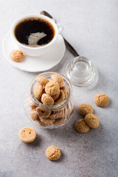 Amaretti cookies in glass pot with white cup of coffee on light gray background with copy space. High angle view