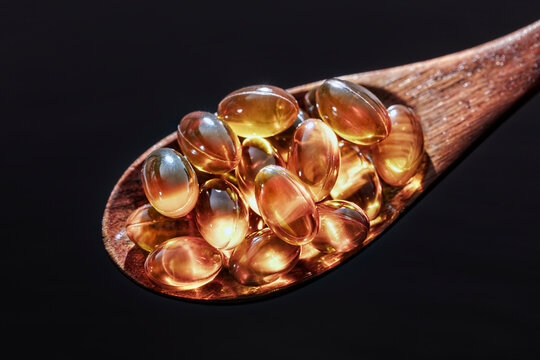 Fish oil capsules with Omega 3 or Vitamin D on a wooden spoon