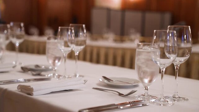 Cinematic footage of an elegant banquet table setting with crystal glassware, silverware, and a microphone, perfect for formal events and weddings.
