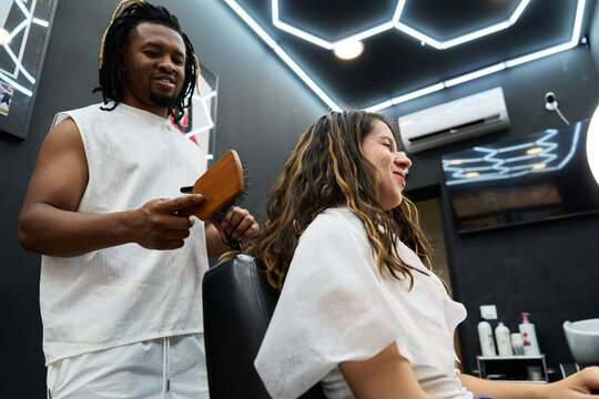 Hairdresser combing female client's long hair in salon