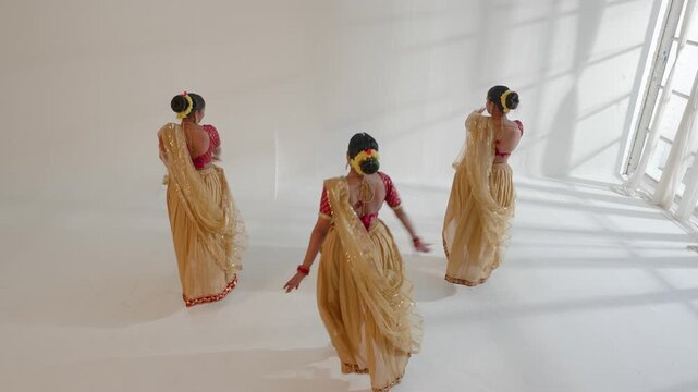 Three Indian women are performing a traditional dance routine in a well-lit studio