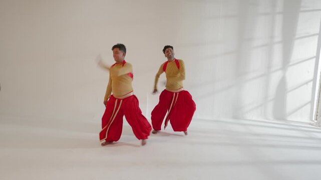 Two Indian male dancers are energetically performing traditional dance moves in a studio