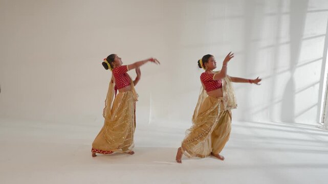 Two women are joyfully performing a classical Indian dance in a studio