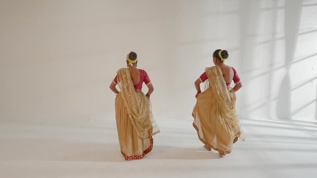 Two women are performing an Indian dance routine in a studio setting