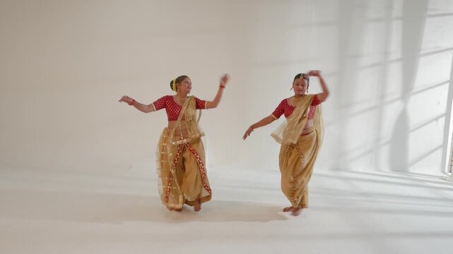 Two women are elegantly performing a classical Indian dance in a studio setting