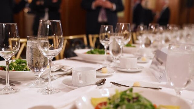 Cinematic footage of an elegant banquet table setting with crystal glassware, silverware, and a microphone, perfect for formal events and weddings.

