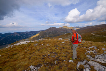 Obraz premium a 75-year-old man hiking in the mountains with poles, a backpack, and mountain gear on a beautiful September day