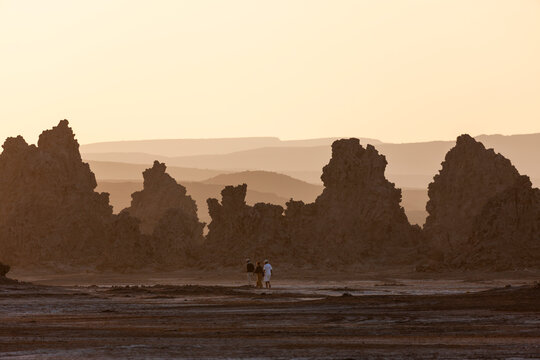 Three tourists walk among towering limestone chimney rock formations at sunset, Afar depression, Lake Abbe, Djibouti