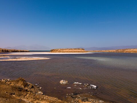 Turquoise water meets white salt flats beneath a distant mountain range, Dikhil Region, Lake Assal, Djibouti