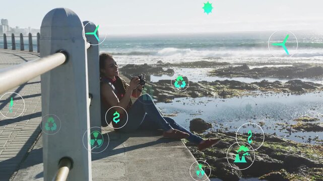 Woman sitting on seawall shooting surf, raising camera and making energy icons drifting around her