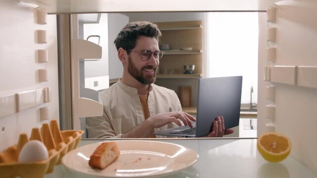 Hungry Caucasian man opening empty refrigerator leftovers food ordering delivery with laptop online shopping supermarket app POV inside fridge male guy buying products groceries meal courier service