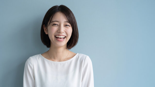青背景の前で満面の笑みを浮かべるショートヘアの女性