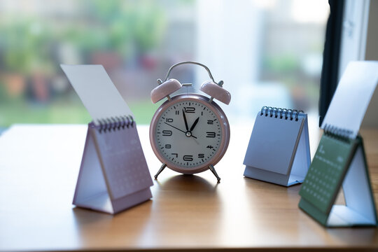 Alarm clock surrounded by desk calendars on a table, representing time management, scheduling, planning, appointments, deadlines and productivity.
