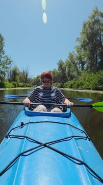 Active adult couple paddling blue tandem kayak along calm forest river in summer