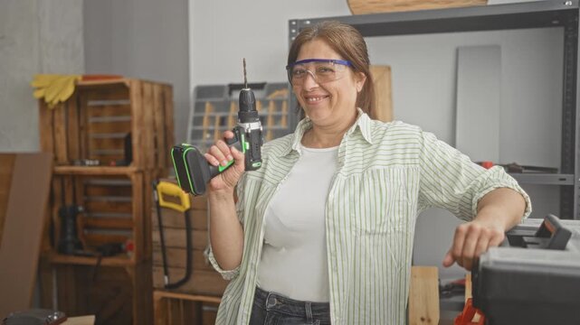 Woman carpenter holding drill in hand in a building workshop, wearing safety goggles and leaning on toolbox; confidence craft pride.