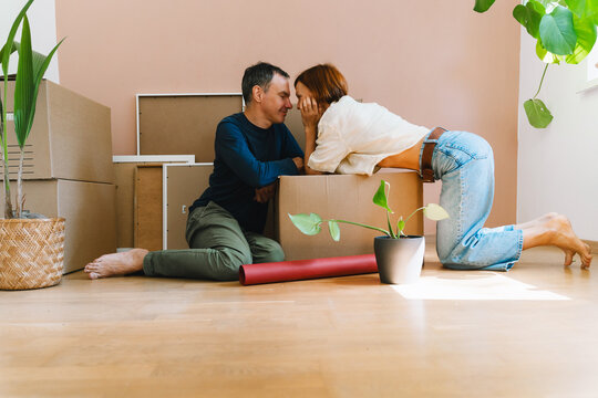 A mature caucasian couple spends time together on the floor surrounded by cardboard moving boxes. Happy family relocation and new property ownership concept.