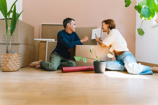 A mature caucasian couple looks at a paper notebook while planning their relocation among moving boxes. Home renovation and family budget planning concept.