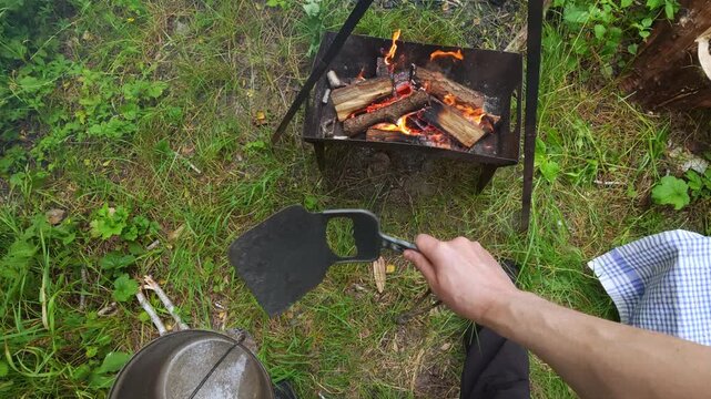 Man fanning charcoal fire with barbecue fan for outdoor camping cooking lifestyle