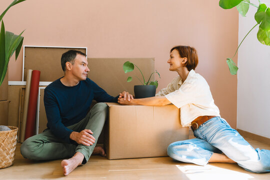 A mature caucasian couple spends time together on the floor surrounded by cardboard moving boxes. Happy family relocation and new property ownership concept.