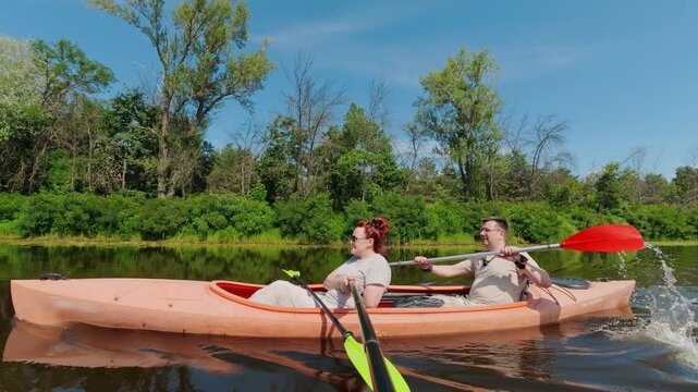 Mature couple paddling orange tandem kayak on a calm river during summer vacation