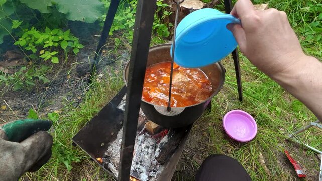 Man pouring water into campfire cauldron for outdoor cooking and picnic lifestyle