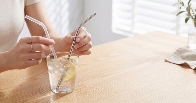 Hands comparing reusable metal straw with disposable plastic straw on wooden table, sustainability concept