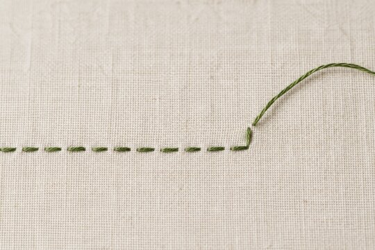 Green running stitches across cream woven fabric