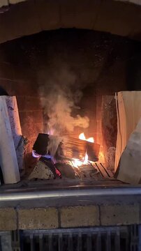 Fire starts burning in a brick fireplace, producing smoke. Effort to warm up a cold home with wood fire, survival concept.