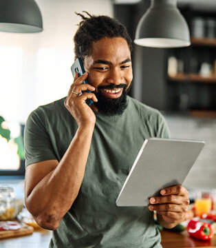 Happy young man having fun preparing food and looking for recipes online using a tablet in kitchen, or a young businessman working from home office making connections online, talking making a phone ca