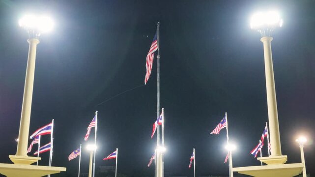 Slow motion zoomed shot of Malaysian national flags (Jalur Gemilang) fluttering on flagpoles against night floodlights at Dataran Putra in Putrajaya, Malaysia.