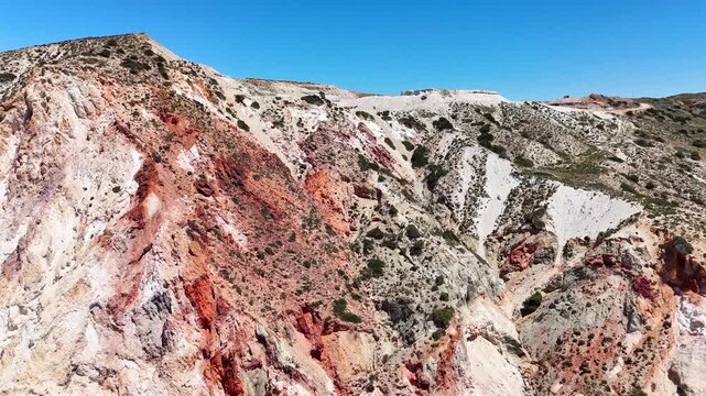 Firiplaka volcanic cliffs expose white, red and ochre tuff with strongly altered rock faces in Milos Municipality, South Aegean, Greece, drone forward flyover