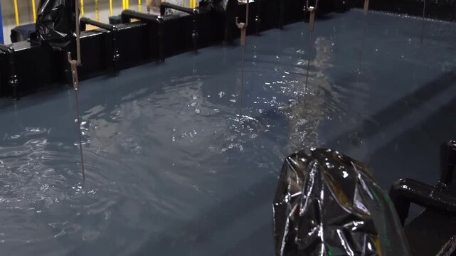 Metal workpieces suspended above a blue chemical pretreatment tank during the degreasing and phosphating stage of a coating line