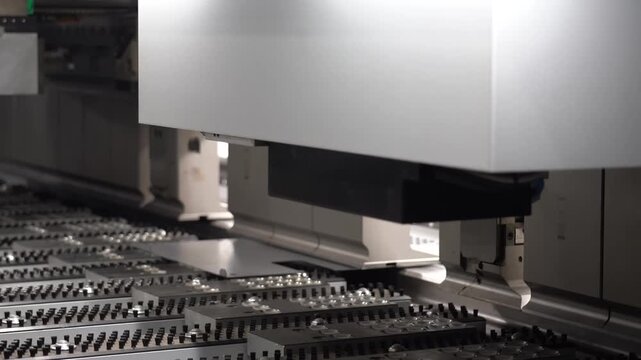 Automated CNC turret punching machine moving over a large metal panel on a ball transfer table in a sheet metal plant