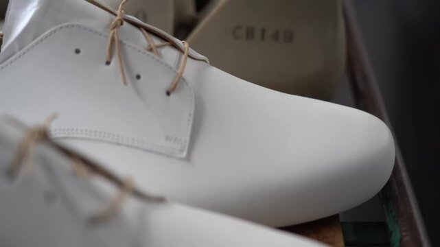 Worker holding a freshly lasted white leather derby shoe still mounted on its plastic last in the workshop
