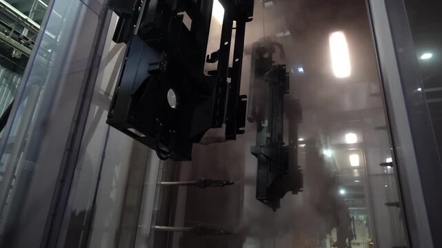 Freshly powder coated black brackets emerging from a curing oven on an overhead conveyor surrounded by rising hot steam