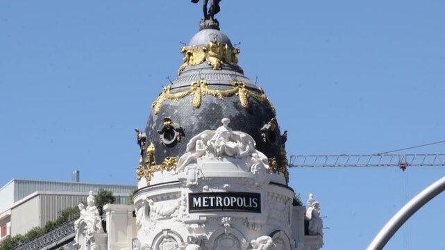 Detailed shot of the iconic Metropolis building dome in central Madrid. Exquisite ornate French-style architecture with gold leaf details against a bright clear sky.