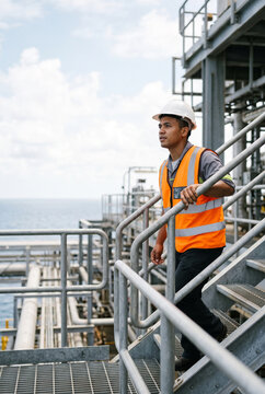 Male worker in safety vest walking down stairs at industrial site  