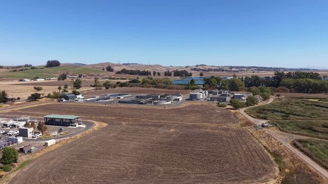 Aerial drone view flying over the Petaluma Water Recycling Facility in California, showcasing the treatment plant, clarification tanks, and surrounding rural landscape on a clear sunny day