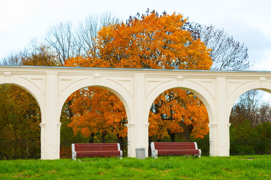 Veliky Novgorod, Russia - Yaroslav courtyard arcade, autumn park background. A white architectural structure with arches and red benches