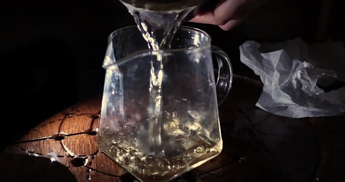 Golden tea filling glass pitcher on carved wooden table in warm evening light