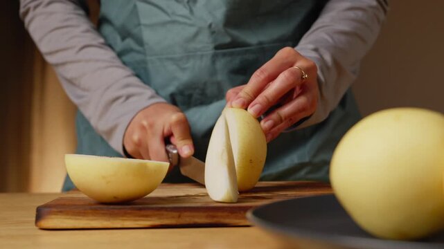 Person cutting a fresh pear in with a kitchen knife on a wooden cutting board