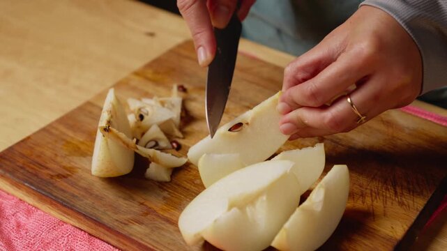 Removing pear core and seed using knife on wooden cutting board